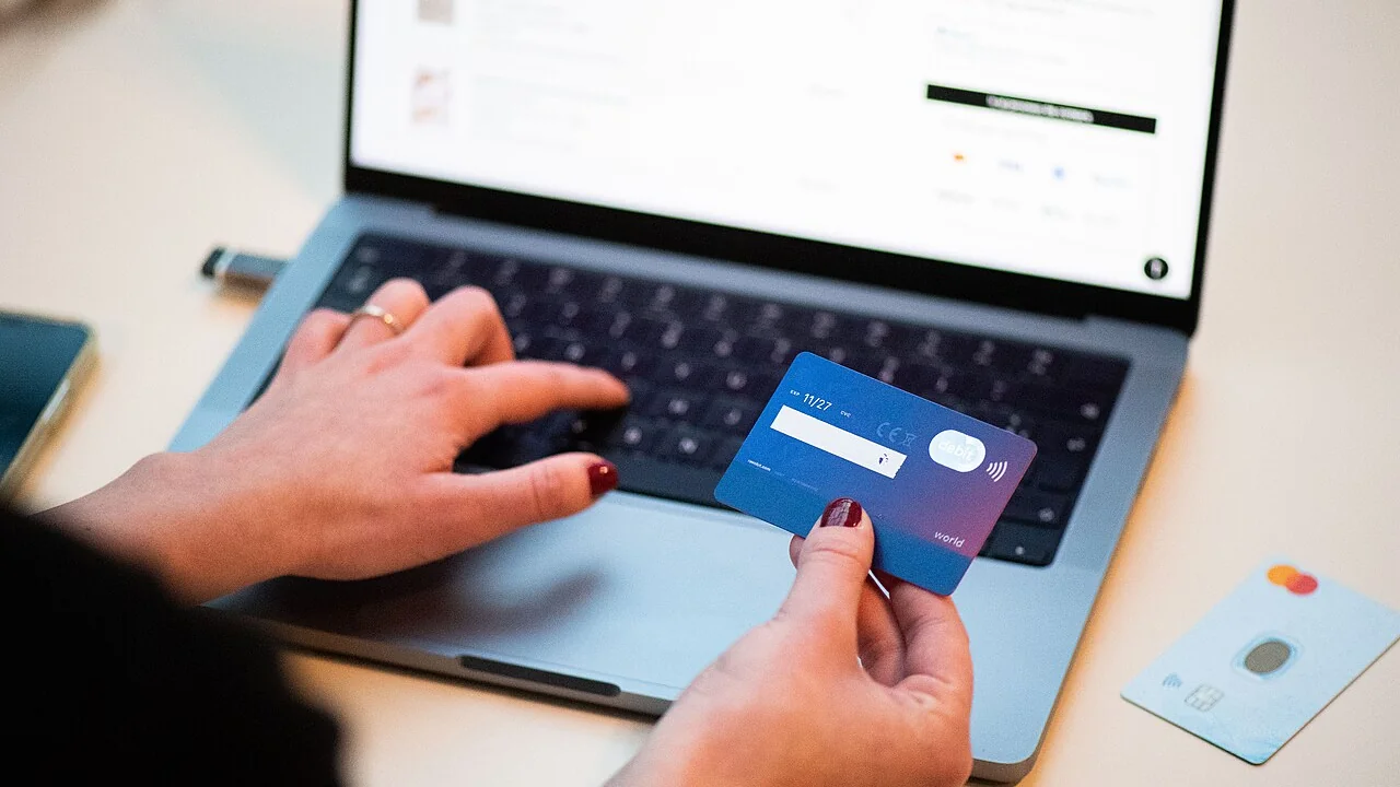 Persona pagando con tarjeta en un portátil durante una compra online, escena de una tienda con datos de clientes